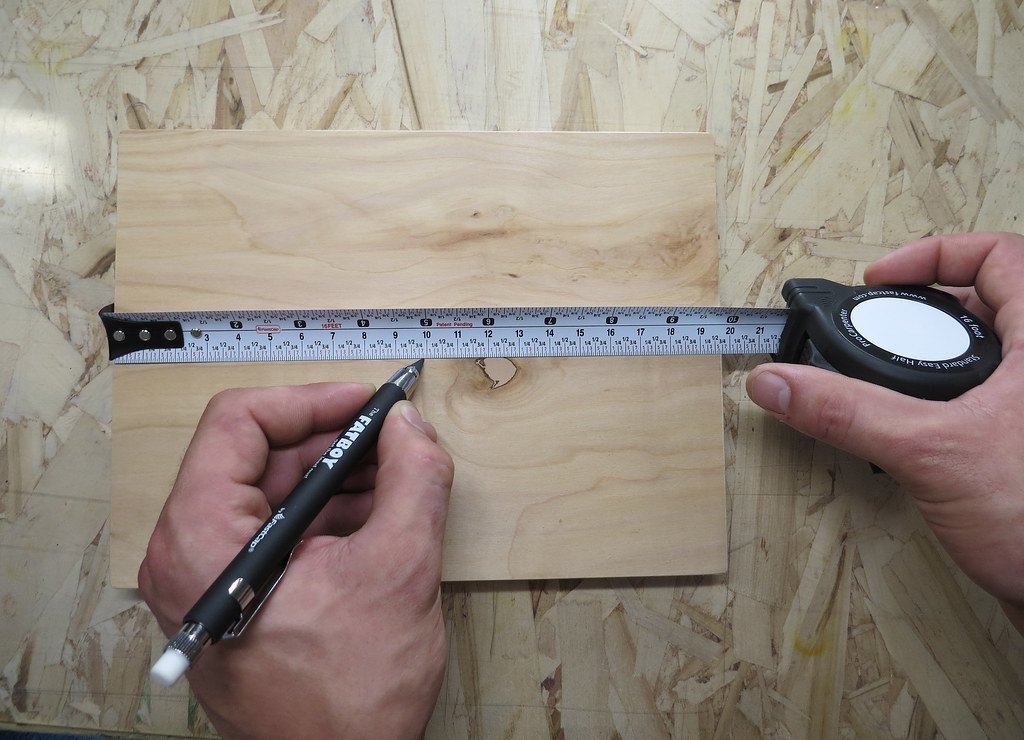 Two hands holding a tape measure across a piece of plywood on a workbench