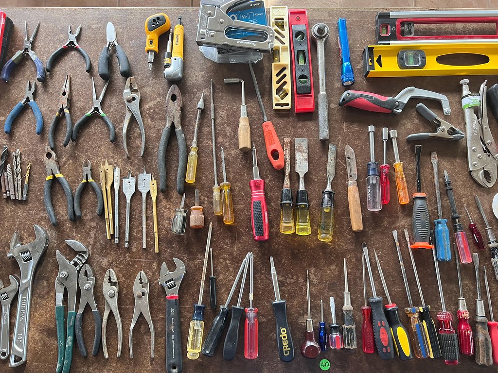 Screwdrivers, pliers, chisels and clamps laid out in rows on a workbench
