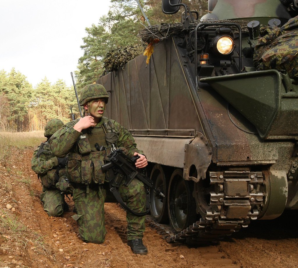 A soldier stepping down from the rear of an armoured tracked vehicle on a dirt track