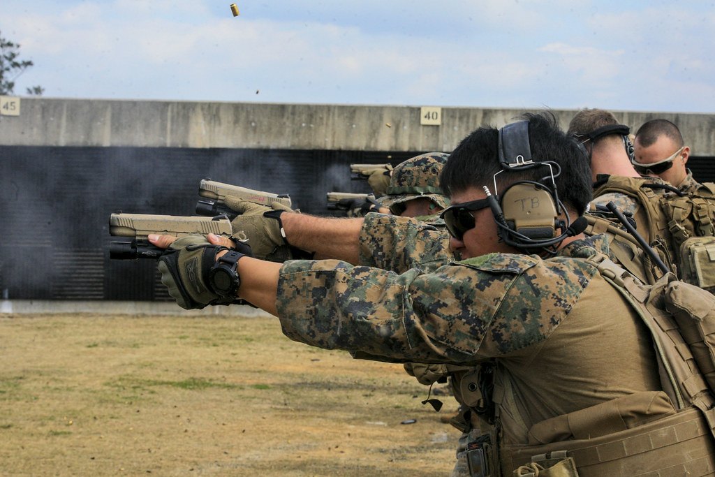 A line of Marines in ear protection firing pistols on an outdoor range
