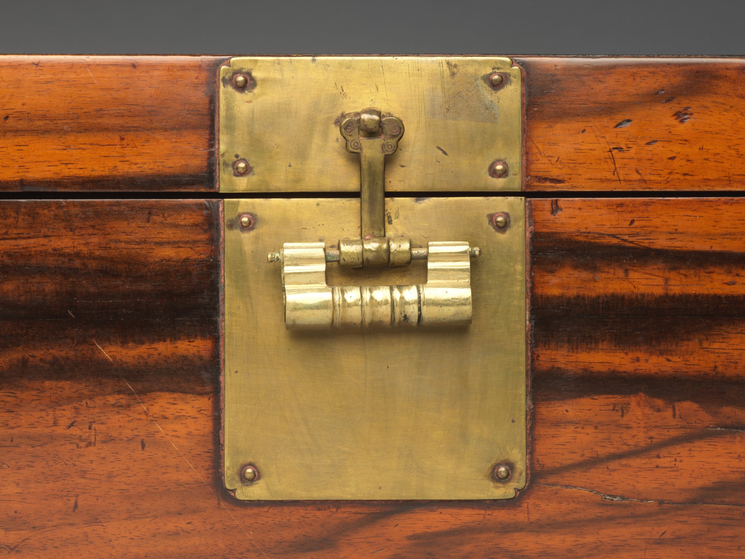 A polished brass lock plate and fitting mounted on a varnished wooden box