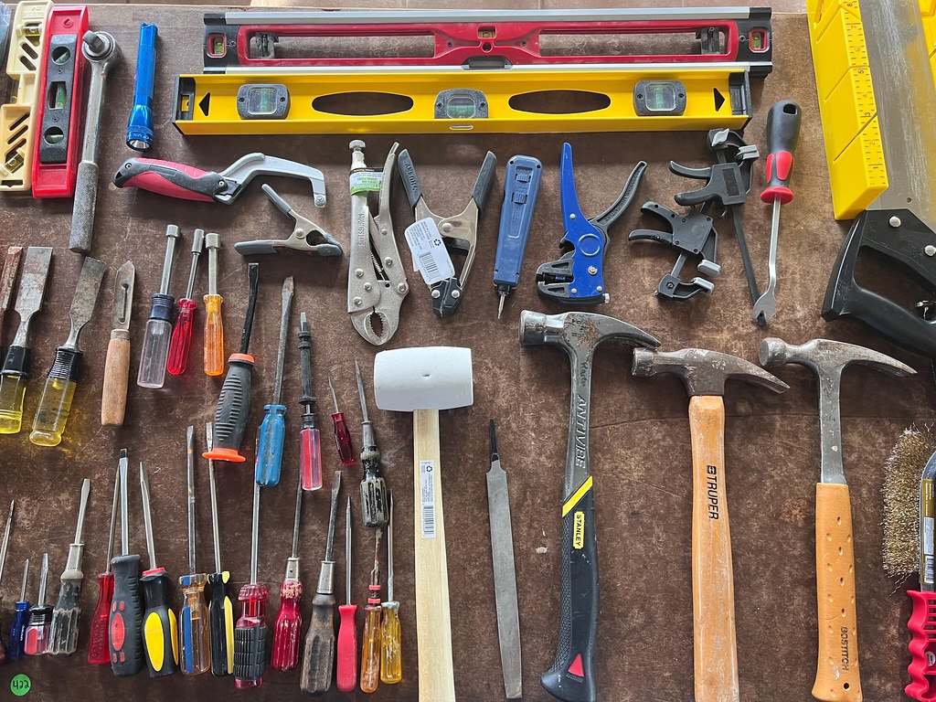 Screwdrivers, files, hammers, clamps and a wire brush laid out in rows on a bench top