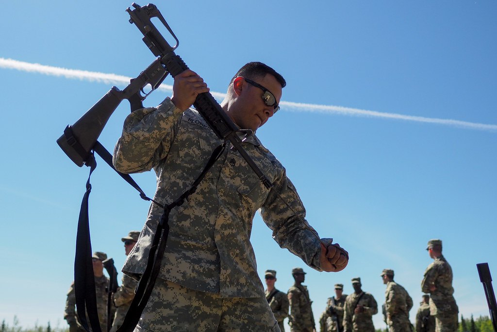 A soldier shouldering a rifle with a black two point sling hanging in a loop from the stock and handguard