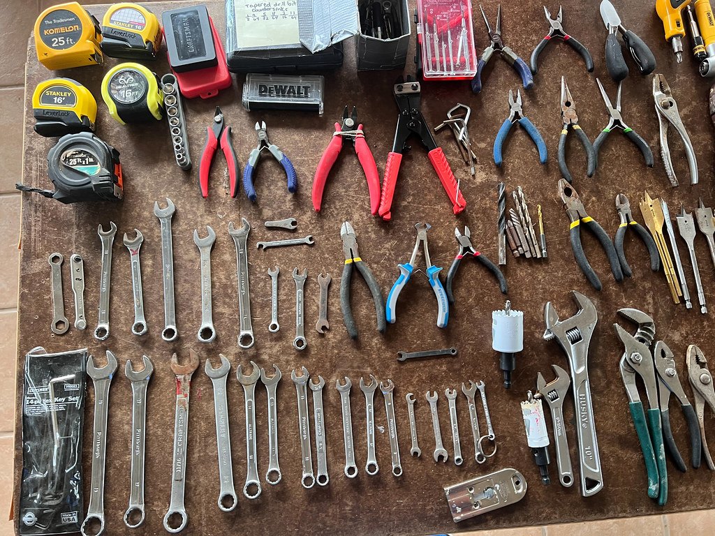 Wrenches, pliers and two tape measures laid out in rows on a bench