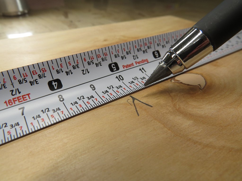 A steel tape measure extended across a sheet of plywood next to a marking pencil