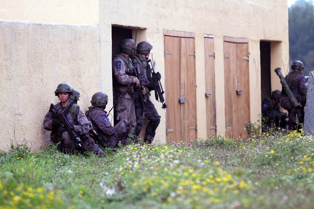 A stack of helmeted personnel holding against a wall next to a row of closed wooden doors