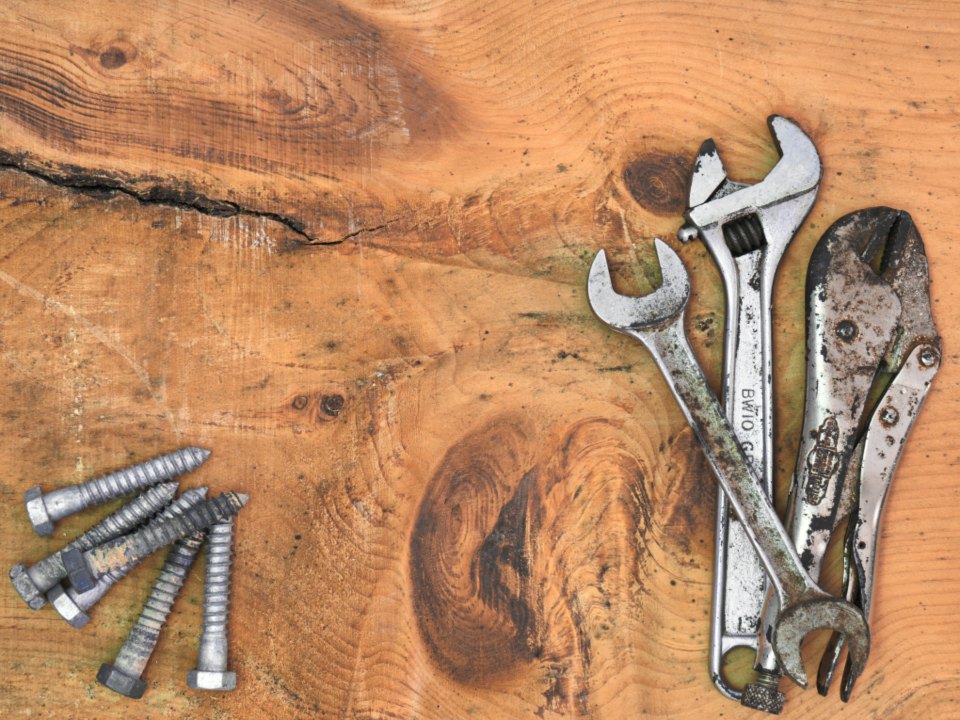 Two spanners and a pair of locking pliers laid on a scarred wooden bench top beside lag bolts