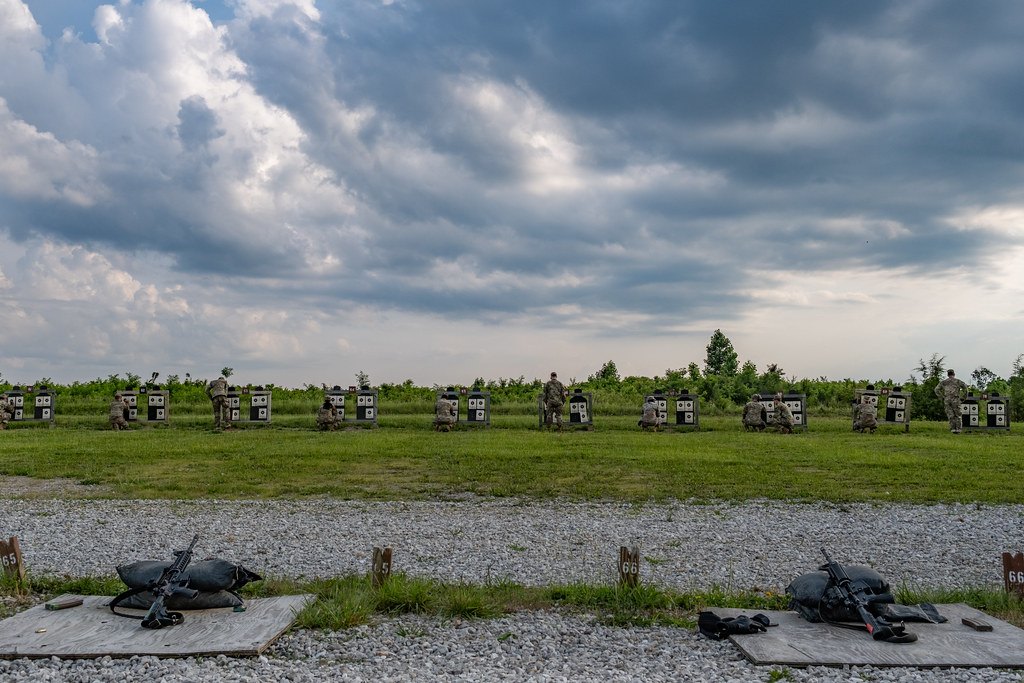 An empty outdoor firing line with rifles laid out on mats and a row of silhouette targets across the grass