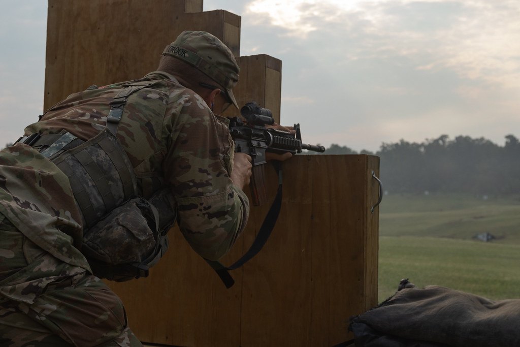 A soldier braced against a wooden barricade aiming a rifle across a misty field