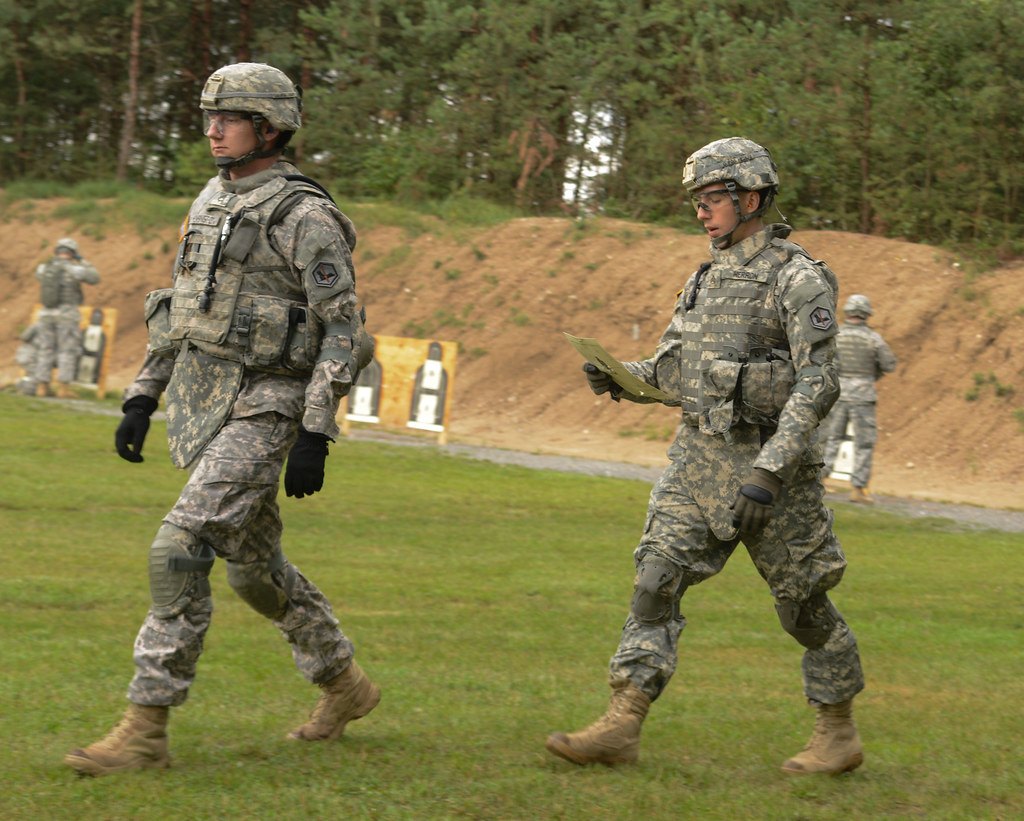 Two soldiers walking down an outdoor range past target frames and a grass berm