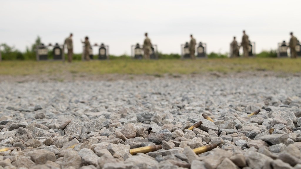 Spent brass cartridge cases scattered on gravel, with a line of silhouette targets blurred in the background