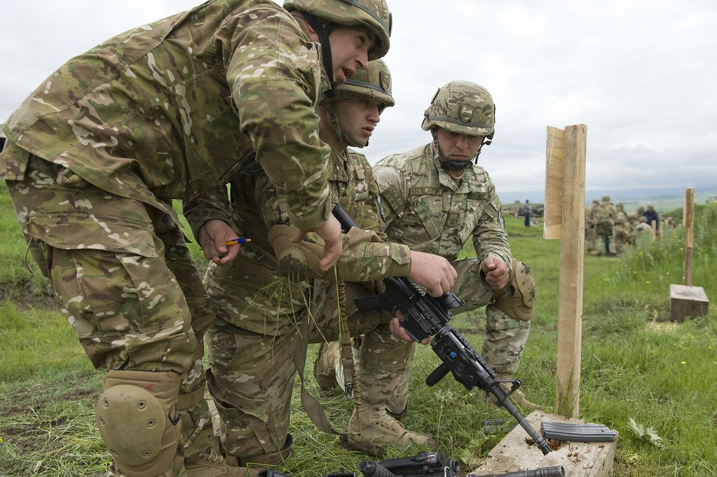 Two soldiers making adjustments to a rifle on a range while a third stands beside them