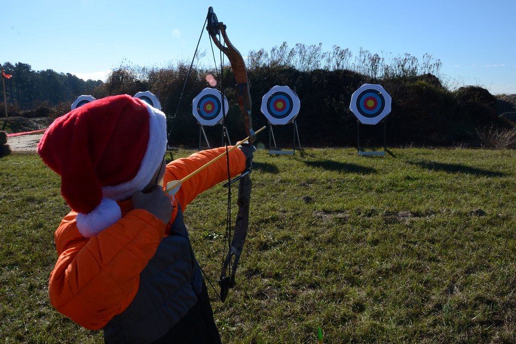 An archer seen from behind aiming at a line of round target faces spaced across a grass field