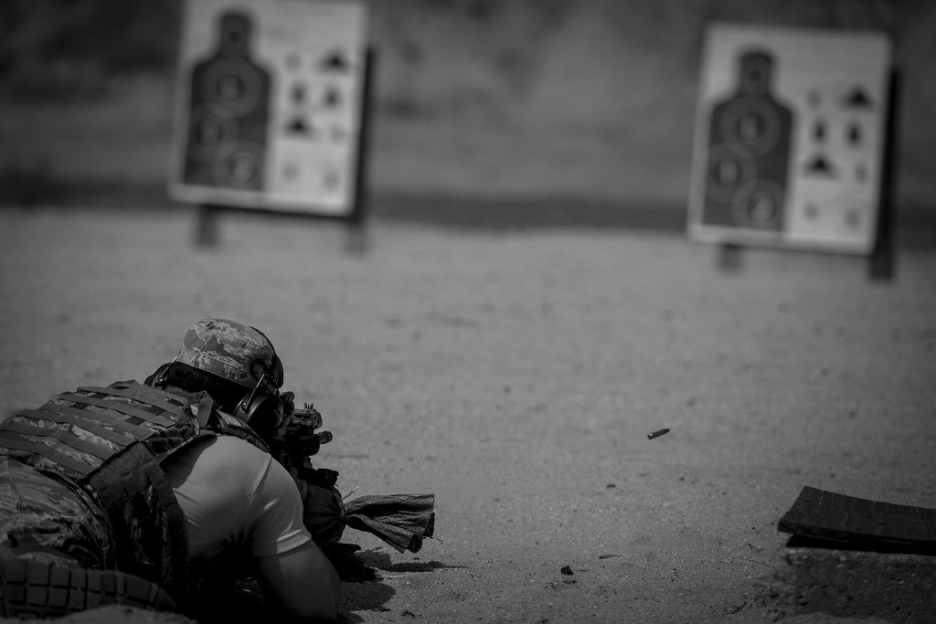 Black and white photograph of a prone shooter on a range with two paper silhouette targets in the foreground