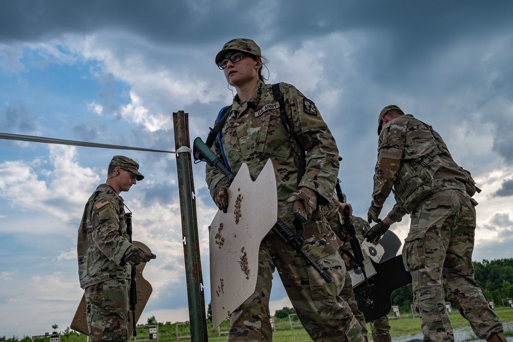 Cadets lifting a silhouette target frame on an outdoor range, their rifles hanging on slings across their bodies