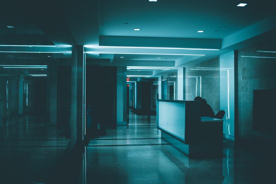 A dimly lit interior at night, with a corridor running past a reception counter under blue-green light