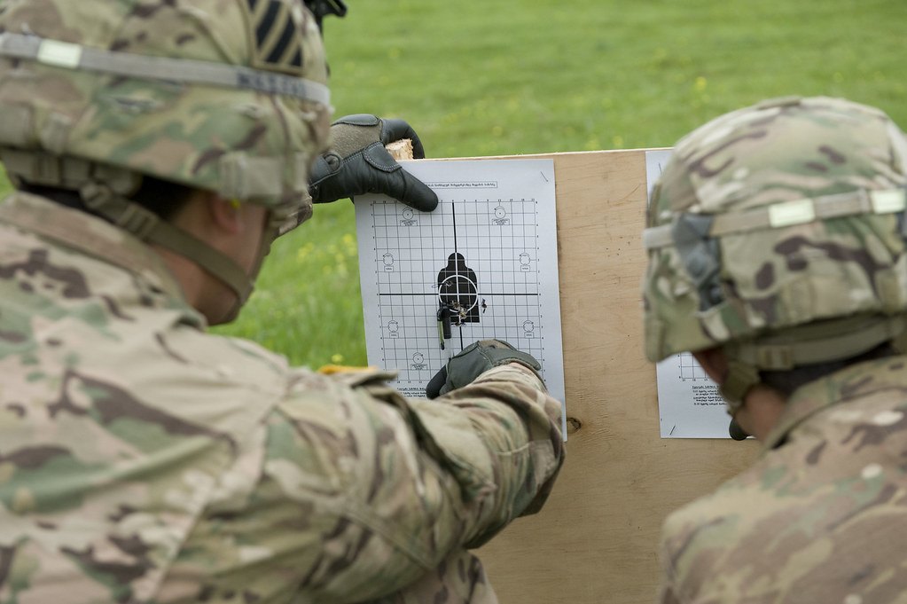 Two soldiers holding a paper zeroing target between them and pointing at the shot holes
