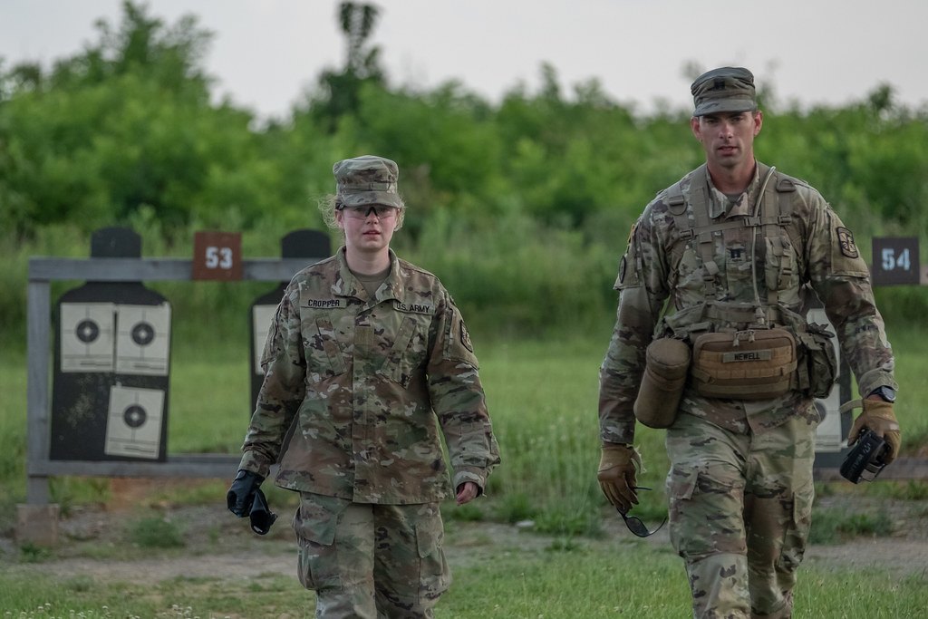 Two soldiers walking along a firing line past numbered paper zeroing targets on wooden frames