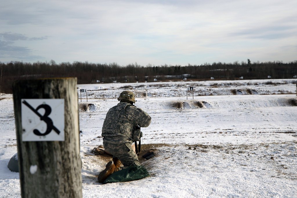 A wooden lane marker post numbered three on a snowy range, with a shooter kneeling downrange