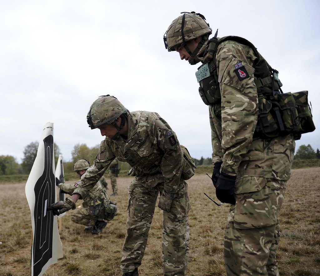 Two soldiers setting up a black silhouette target frame in an open field