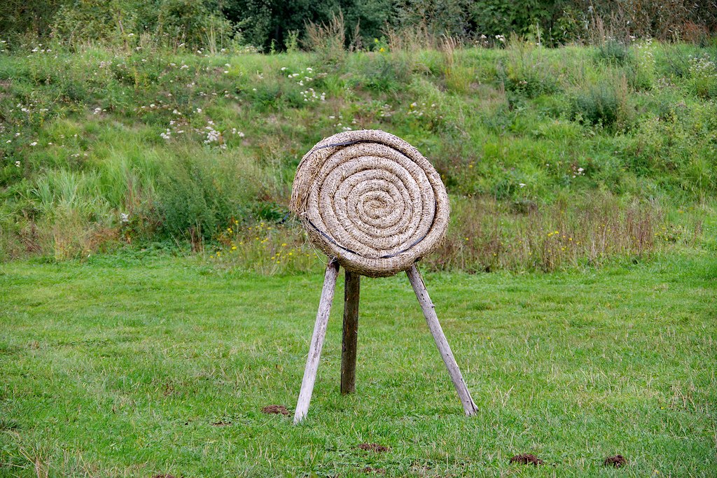 A round straw archery butt on a wooden tripod standing in a grass field