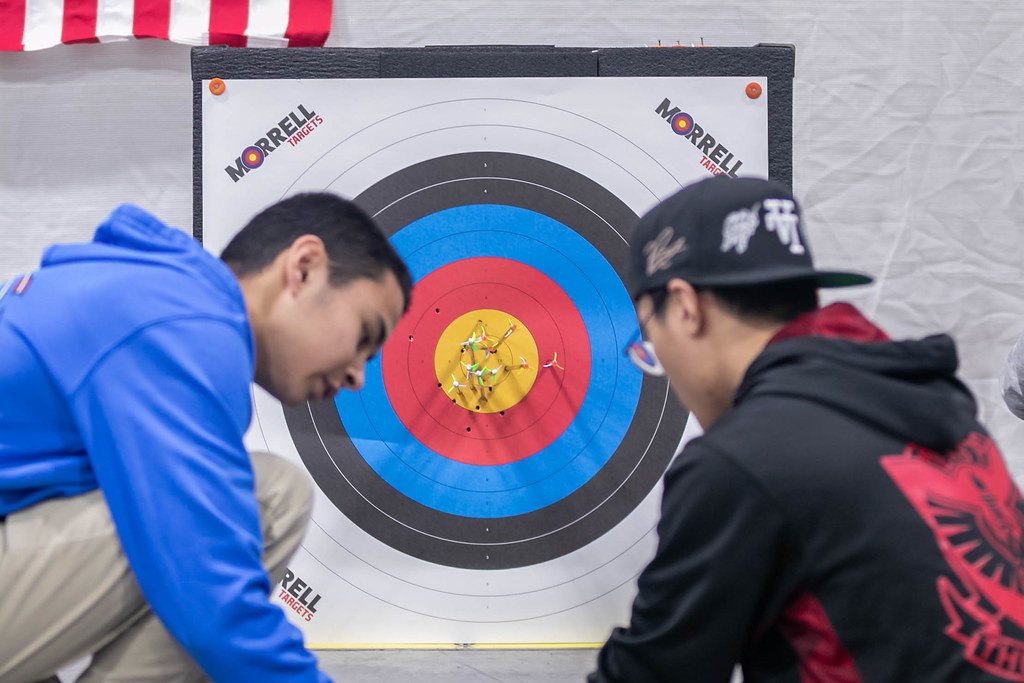 Two archers leaning in to pull arrows from a target face on an indoor range