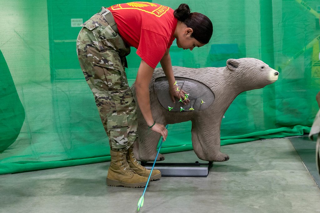 A person adjusting a life-size three dimensional bear target with an arrow standing in the ground beside it