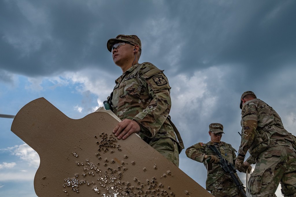 A soldier holding up a silhouette target covered in shot holes and pasters