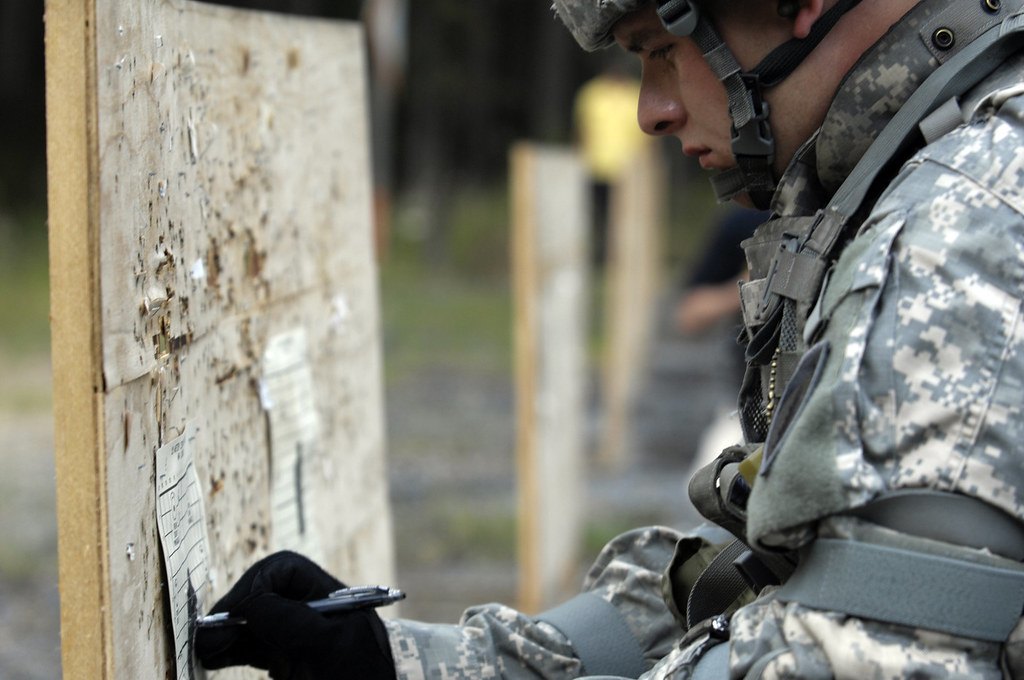 A soldier marking shot holes on a paper target pinned to a wooden backer board