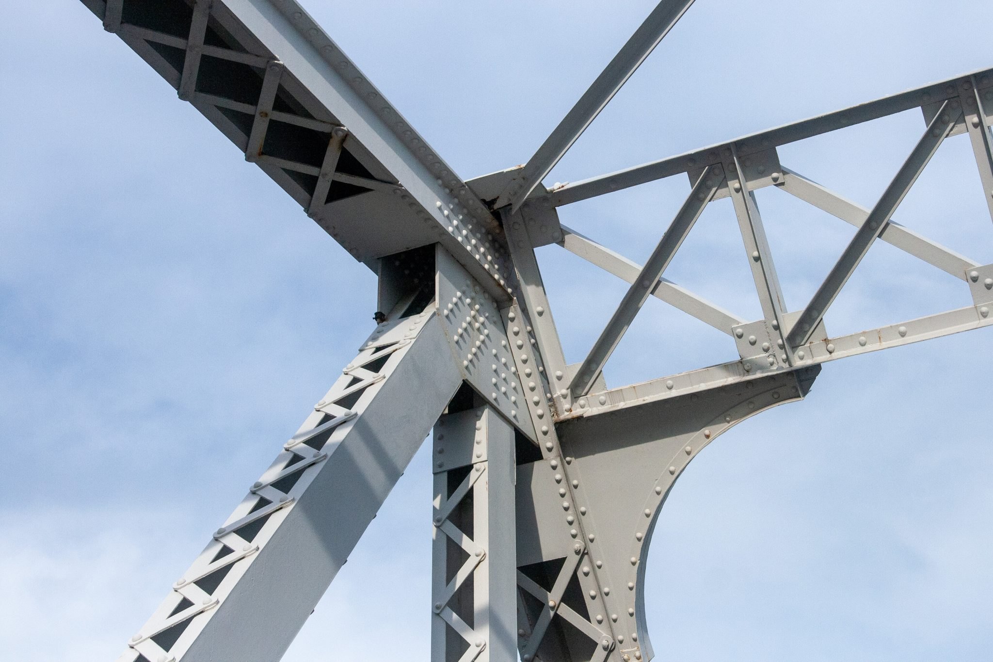 The underside of a steel bridge showing a riveted gusset plate joining several beams
