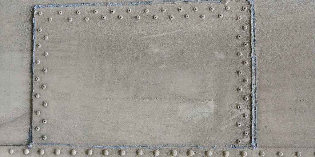A welded and riveted steel panel with a visible seam running around its edge
