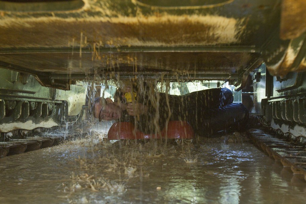 A worker lying underneath a tracked vehicle as muddy water pours down around them
