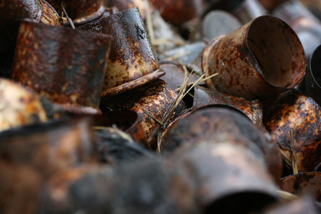 A pile of spent shotgun shell heads on the ground, the metal bases rusted brown