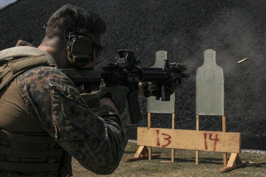 A shooter at a range firing a semi automatic rifle with a spent case in the air beside the ejection port