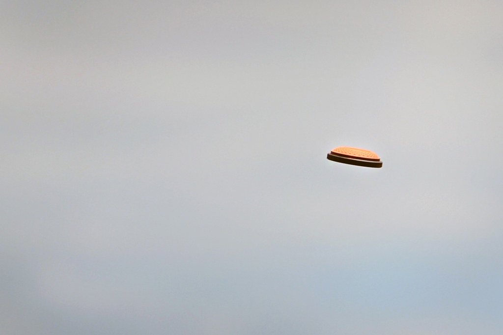 A single orange clay target flying against a pale overcast sky