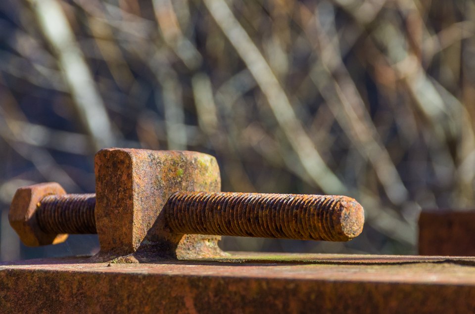 A rusted bolt and clamp seized onto a rusting steel bar outdoors