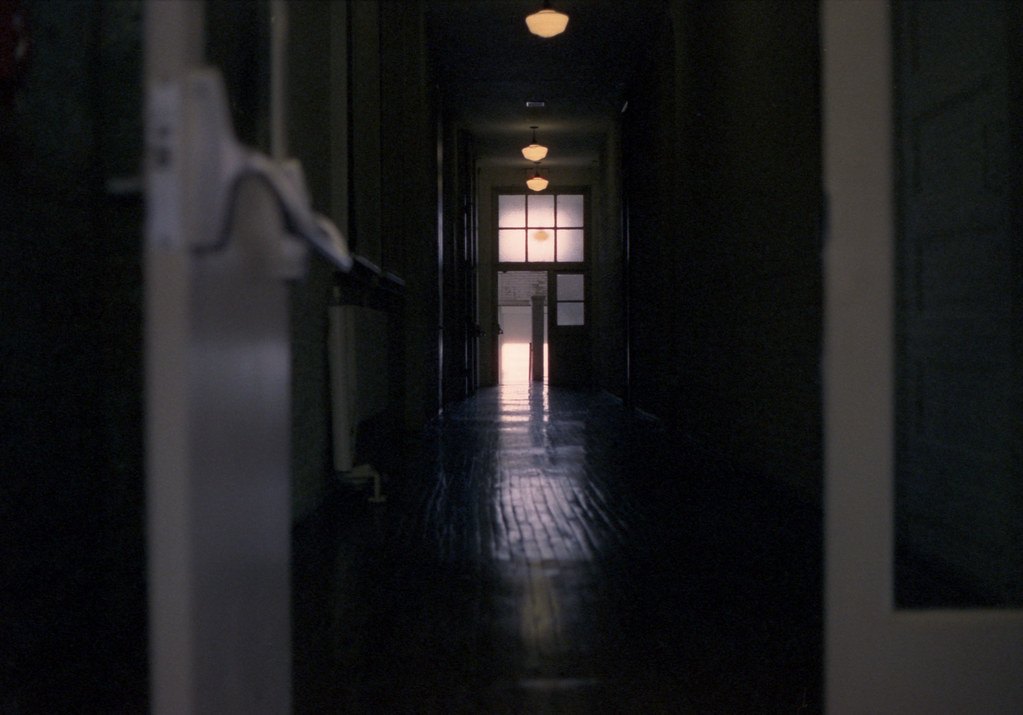 A dark interior hallway with wooden floor and a lit glass door at the far end