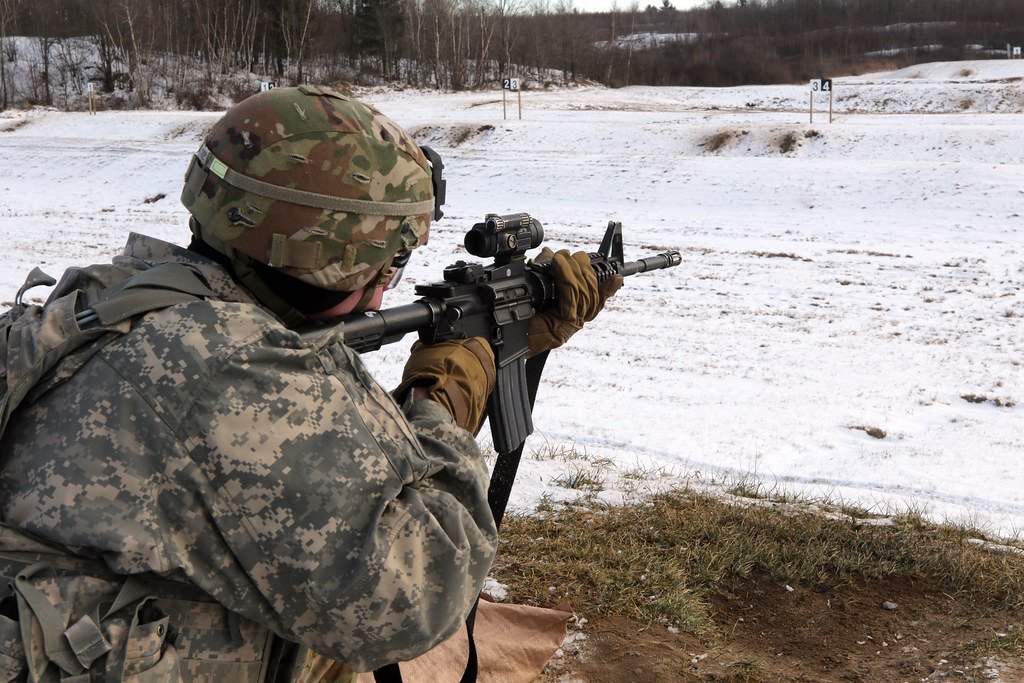 A soldier kneeling on a snow-covered range aiming a rifle fitted with a small optic