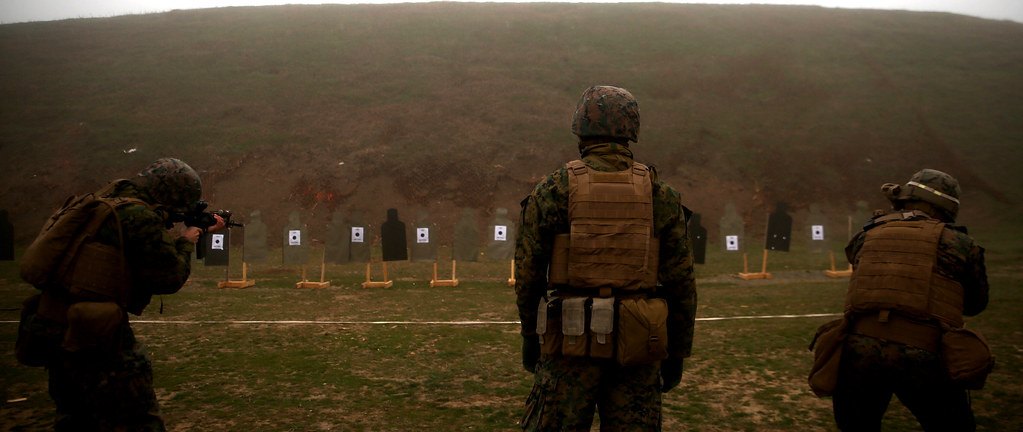 A covered firing line with shooters prone and silhouette targets set out downrange