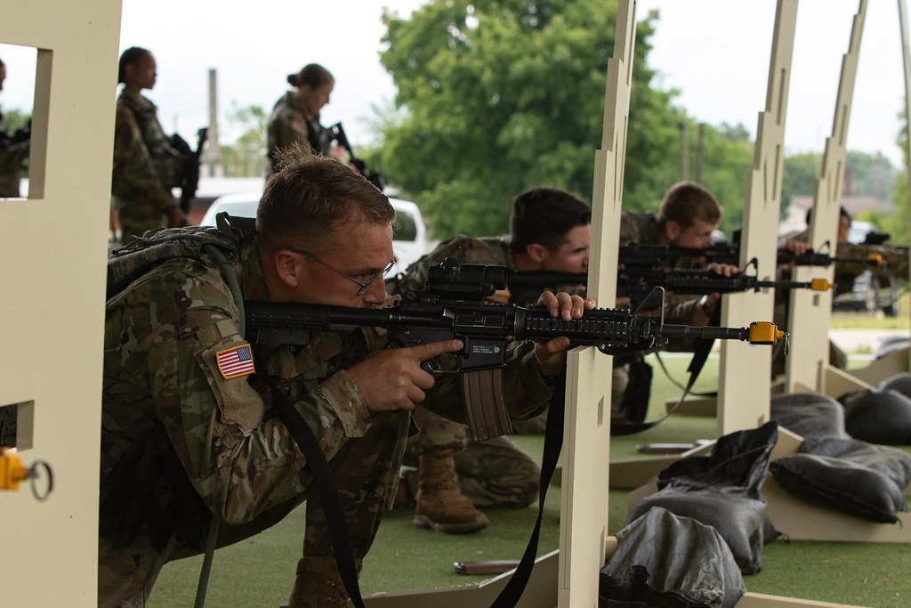 Shooters lined up under a covered firing point, rifles up and slings hanging from them
