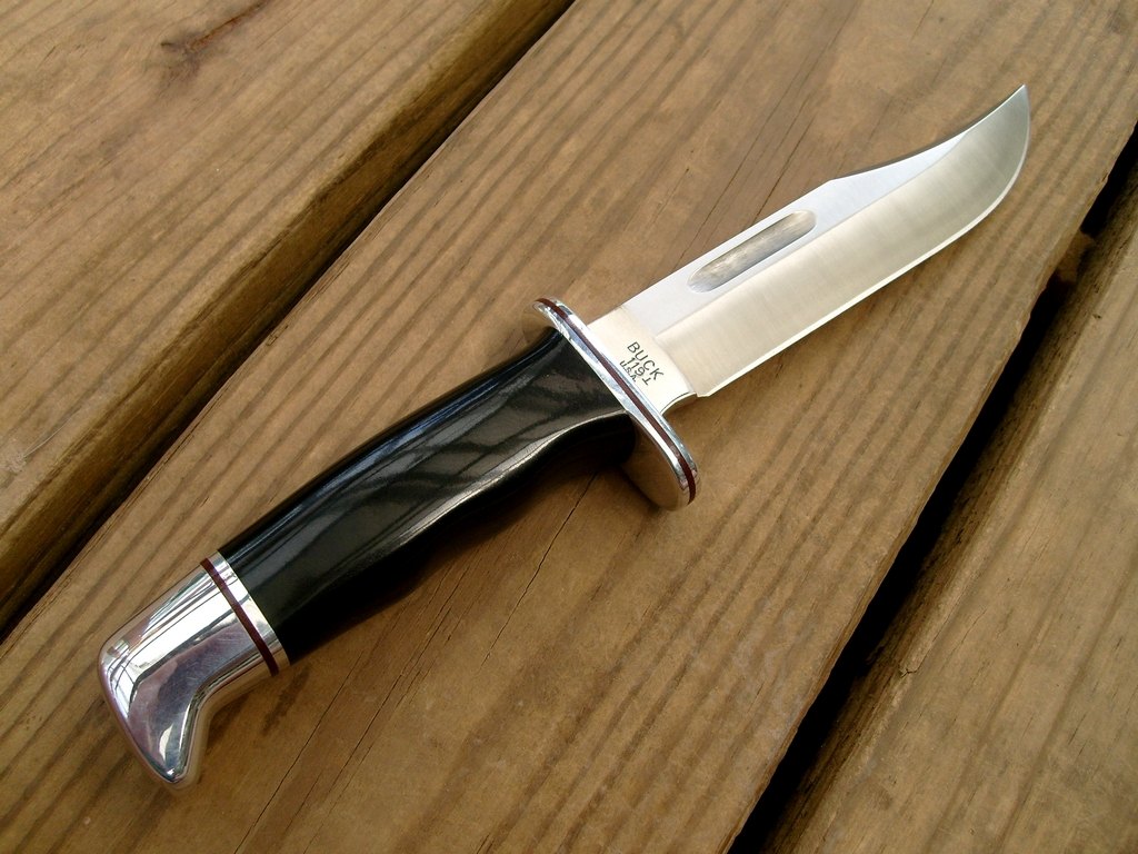 A fixed blade hunting knife with a dark handle lying on weathered wooden boards