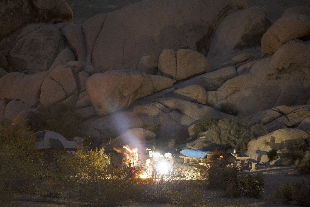 A lit campsite at night among large rounded boulders, with a tent and a fire