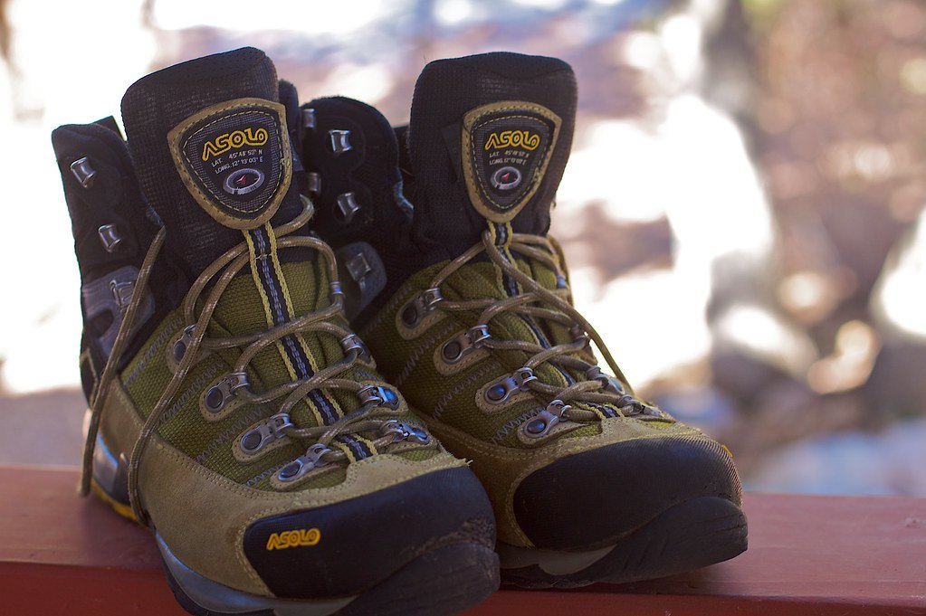 A pair of worn leather and nylon hiking boots standing on a wooden rail