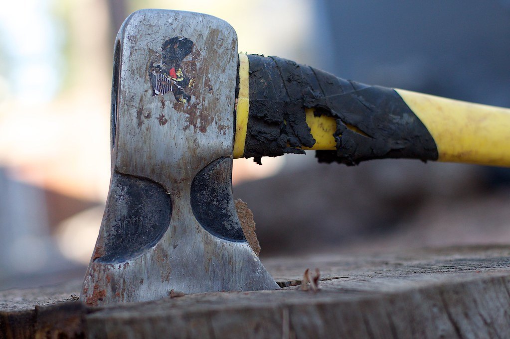 A worn axe head with a chipped painted handle resting on a chopping block