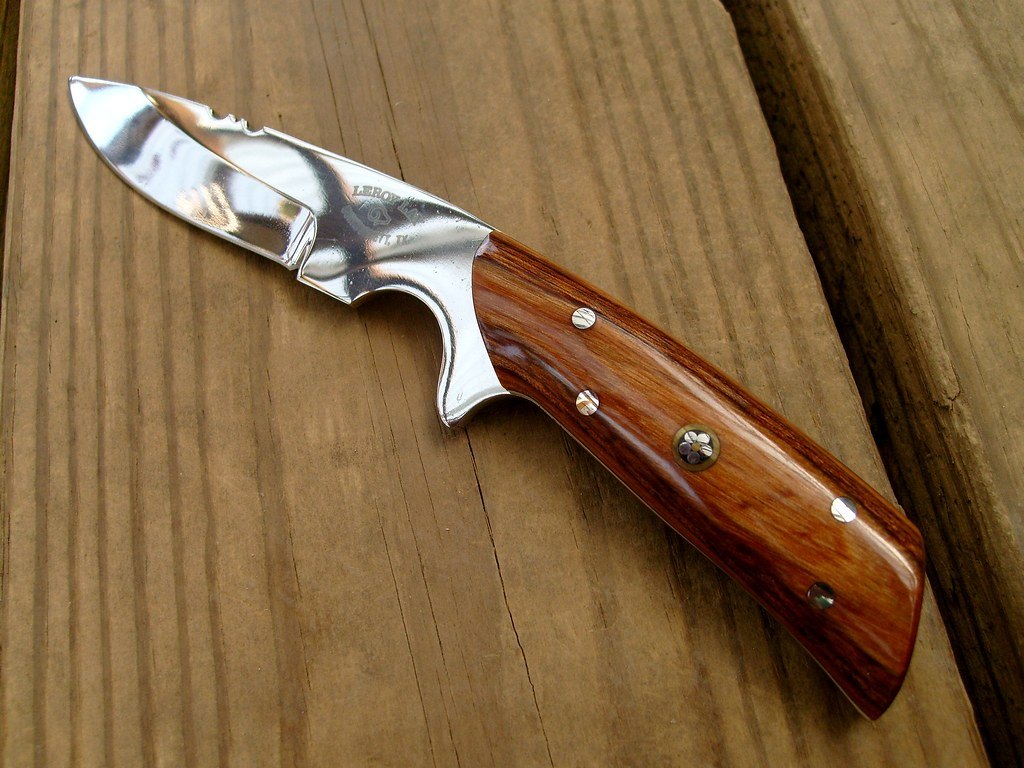 A small custom hunting knife with a polished blade and a wooden handle on weathered boards